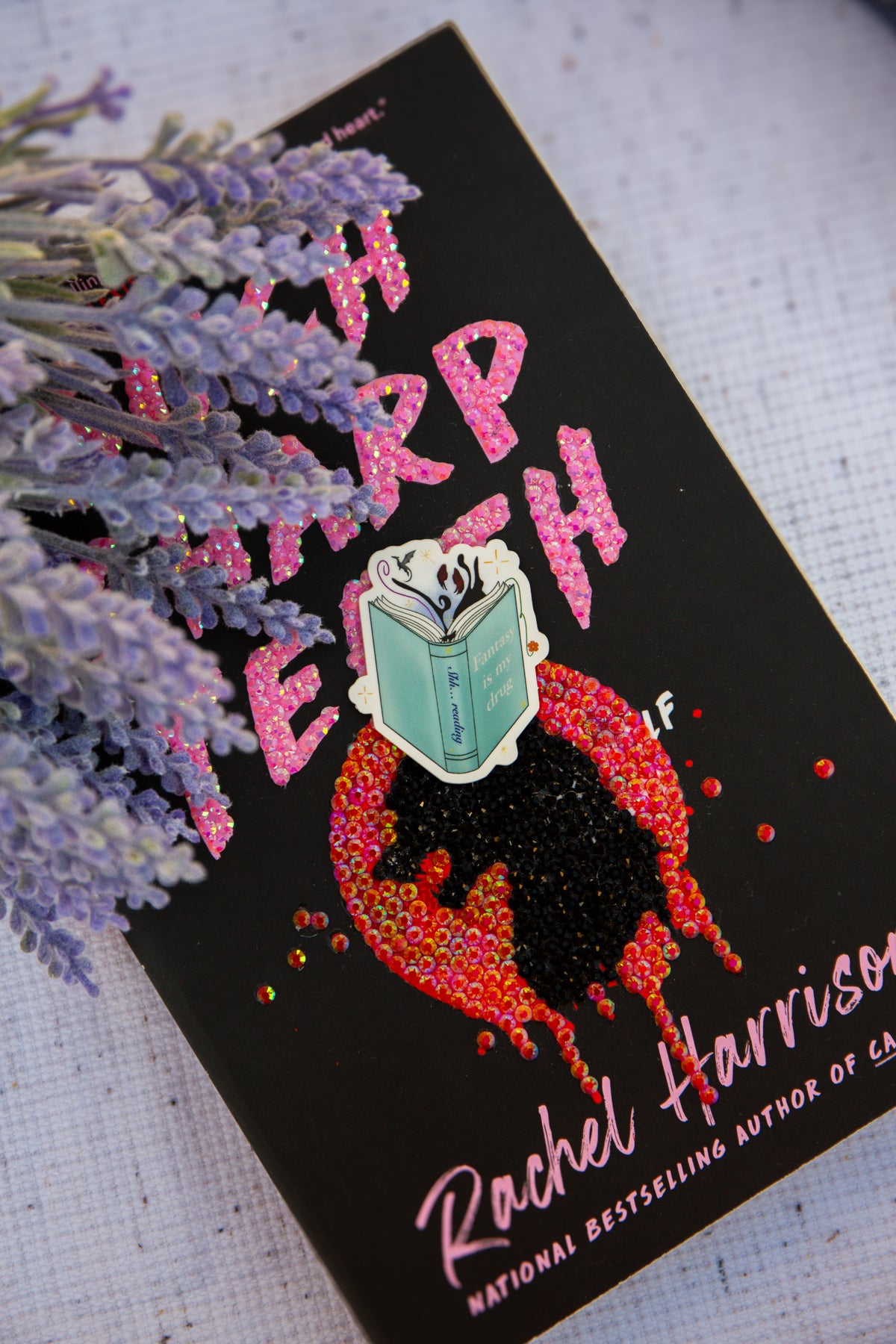 Book titled 'such sharp teeth' by Rachel Harris with sticker product on top and lavender flowers.