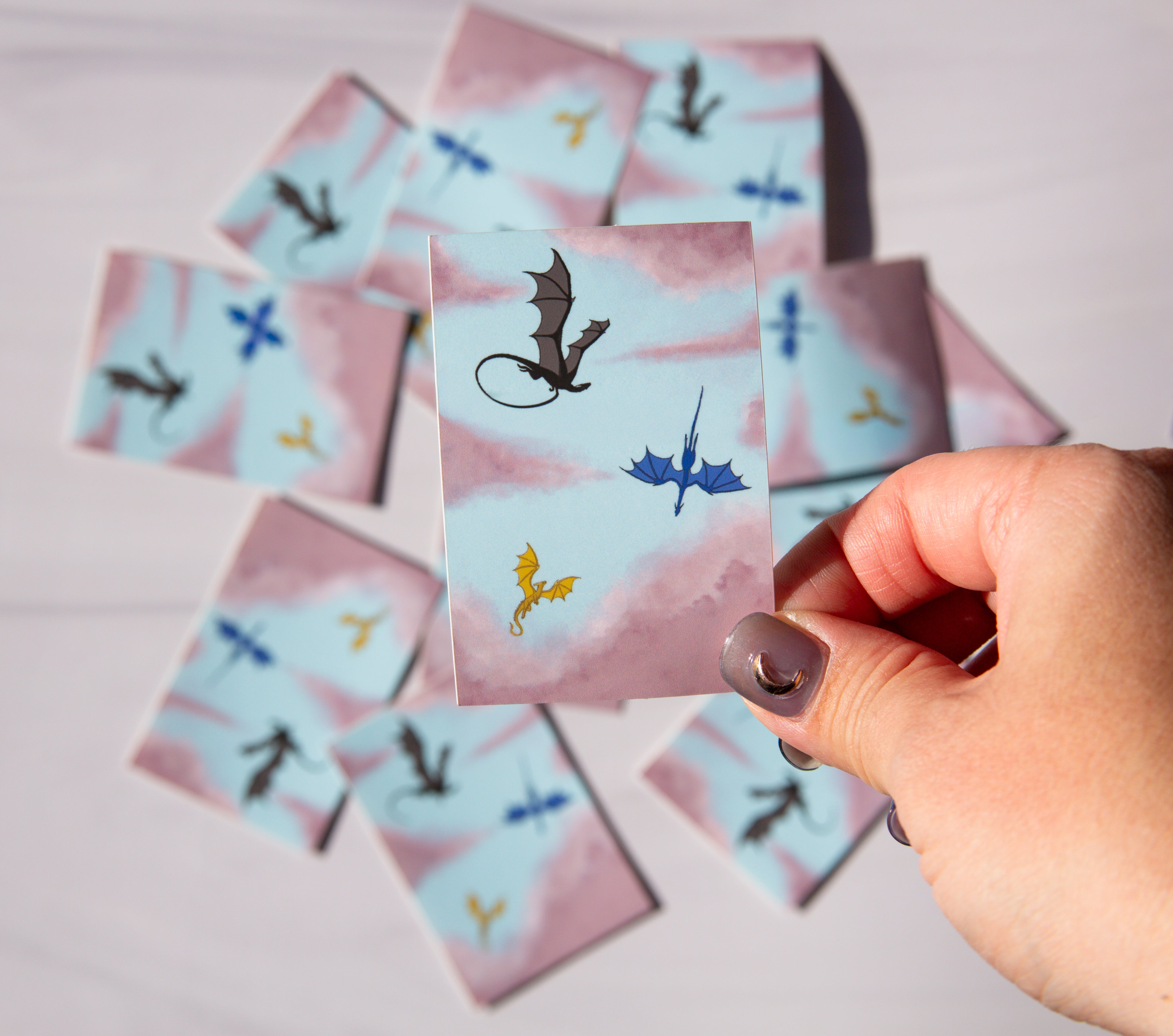 Hand holding a card with dragon illustrations on a pink and blue background