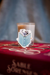 a small candle with a sticker of a book on top, placed on a red book