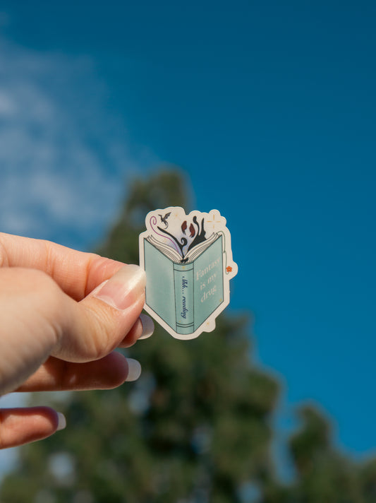 Hand holding a sticker with a book design against a blue sky