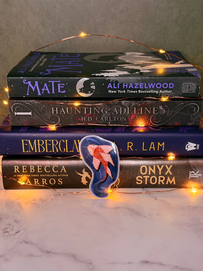 Four books titled 'Mate', 'The Haunting of Hill House', 'Onyx Storm', and 'Emberclan' on a marble surface with string lights.